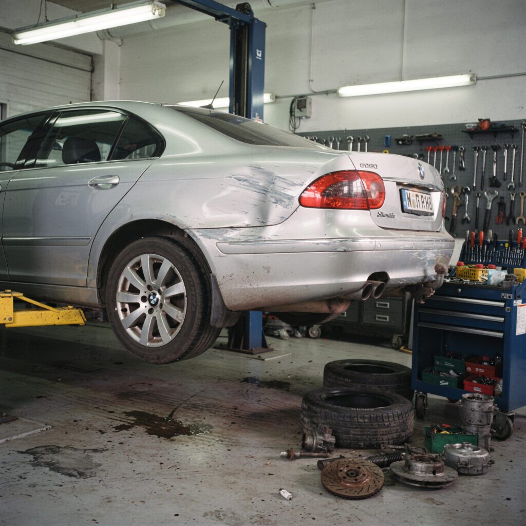 Deformierter Kotflügel eines silbernen Autos auf einer Hebebühne in einer Kfz-Werkstatt.